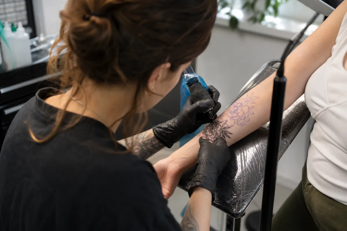 Tatoueur de dos concentré sur un motif floral dans un studio lumineux