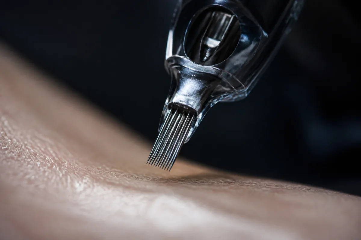 Aiguille de tatouage en gros plan au-dessus d&rsquo;une peau tendue, atelier faiblement éclairé